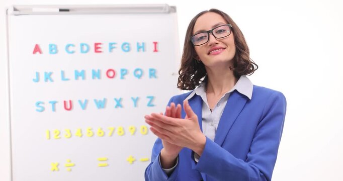Lady teacher claps hands in front of alphabet board at classroom presentation. Educator brings palms together praising progress with confident smile