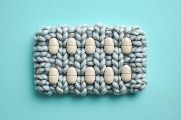 realistic studio photo of a medicine blister pack made of silver and white chunky wool yarn with cozy pharmacy and treatment concept on teal background