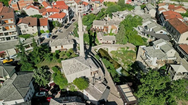 Mostar, Bosnia and Herzegovina - 05 28 2025: Angled drone video of Hajji Kurts Mosque with Hamam Museum to the right and Neretva River in the background in Mostar Old Town on a sunny day.