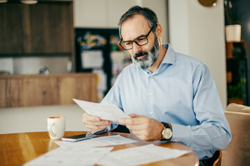 Mature man analyzing financial documents at home