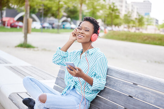 Portrait of young woman sitting on bench listening music with cell phone and headphones