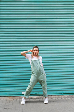Cool young woman making hand sign in front of blue roller shutter