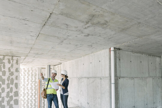 Male architect and female manager talking about architectural plan at construction site