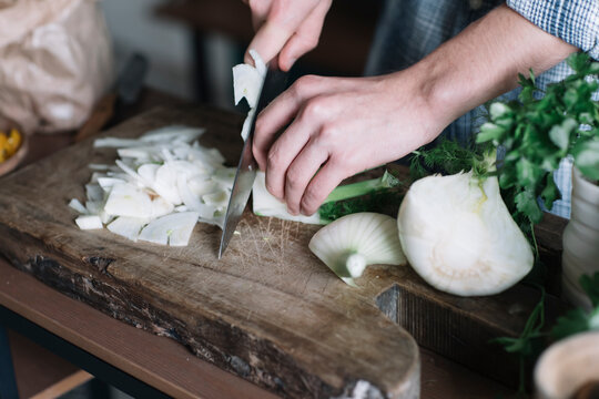 Hands of man cutting fennel on board in kitchen