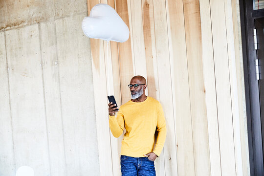 Mature businessman holding cell phone attached to cloud balloon