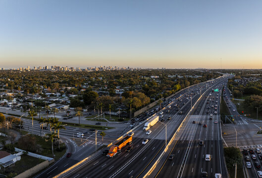 Aerial view of the I-95 highway cutting through a vibrant tapestry of city streets and lush greenery under the soft glow of the setting sun, Hollywood, Florida, United States.
