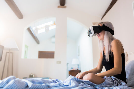 Young woman sitting in bed wearing VR glasses