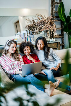 Three happy women with laptop sitting on couch