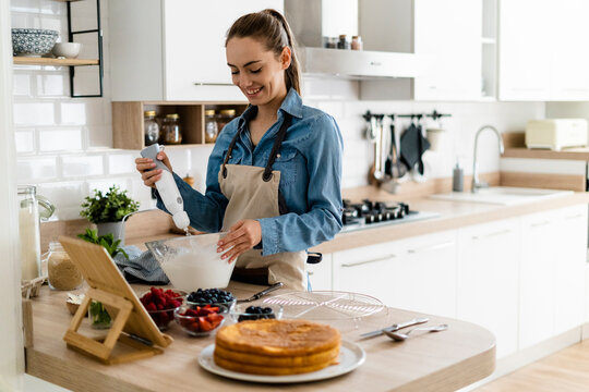 Young woman preparing a cream cake, using tablet