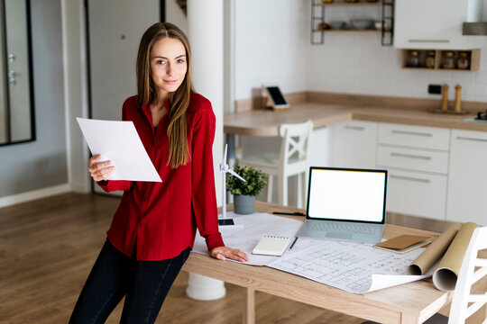 Portrait of smiling woman in office holding paper with wind turbine model on table