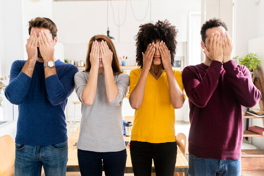 Four friends standing side by side at home covering their faces