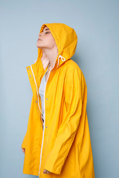 Young woman wearing yellow rain coat in front of blue background