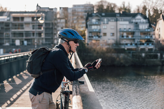 Senior man with cyclist helmet using smartphone on bridge