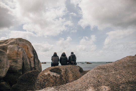 France, Brittany, Meneham, friends sitting on rock formation at the coast