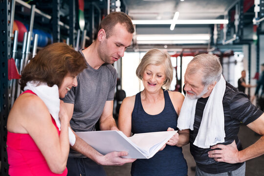 Group of fit seniors and personal trainer in gym looking in folder