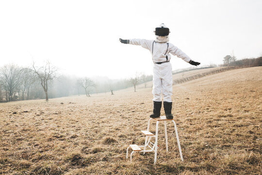 Boy wearing white space suit with raised arms on a step with virtual reality glasses