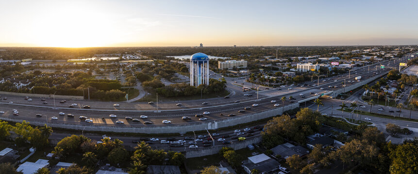 Aerial view of the city's arteries pulse with life around a towering water tower, bathed in the warm glow of the setting sun, Sunrise, Florida, United States.