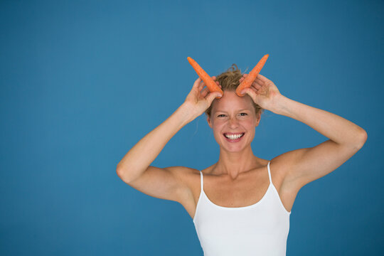 Smiling blond woman holding carrots, blue background