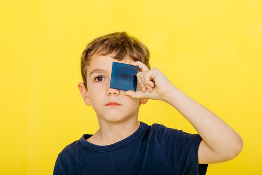 Close-up of cute boy holding blue acrylic glass against yellow background