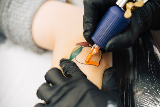 Female tattooist tattooing a peach on a woman's arm