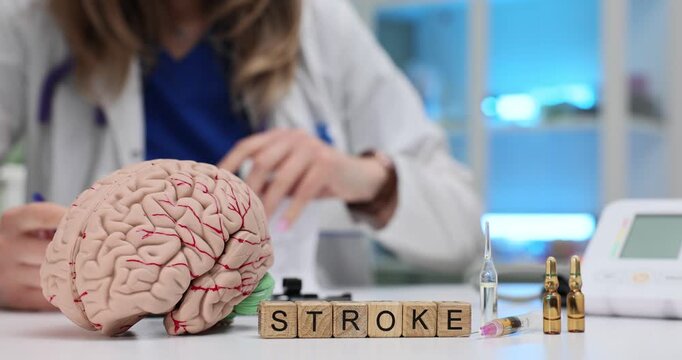 Wooden blocks spell word Stroke near brain model and ampoules on desk. Female doctor studies brain reviewing emergency protocol for fast response