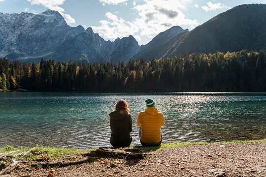 Rear view of couple sitting on lakeside at Laghi di Fusine, Friuli Venezia Giulia, Italy