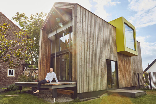 Mature man with beer bottle sitting outside tiny house during summer