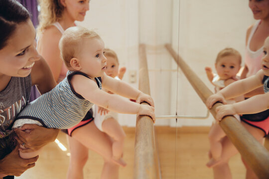 Two mothers holding up their small children to barre in dance studio