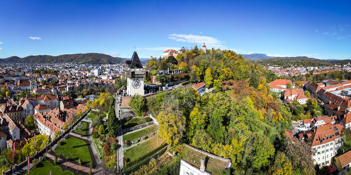 Aerial view of the Grazer Uhrturm clock tower on Schlossberg hill amidst a tapestry of autumnal colors under a clear sky, Graz, Styria, Austria.