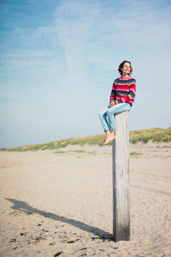 Mature woman sitting on a wood pole on the beach