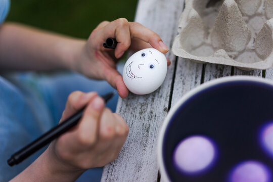 Close-up of girl painting face on Easter egg on garden table