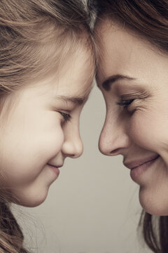 close-up vertical portrait of mother and daughter touching foreheads and smiling, soft neutral background, gentle natural light, emotional bonding moment
