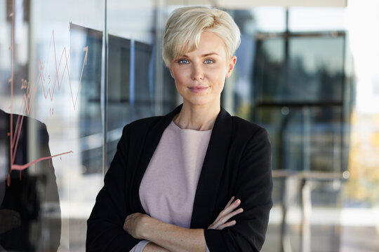 Portrait of confident businesswoman next to chart on glass pane in office