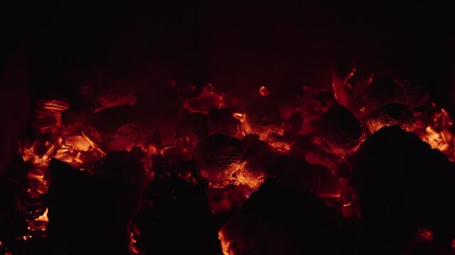 Flames dance amid glowing embers in a charcoal firepit at night