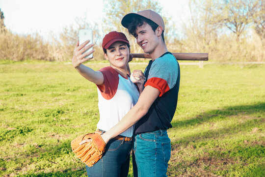 Smiling young couple with baseball equipment taking a selfie in park
