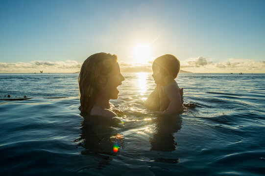 French Polynesia, Tahiti, Papeete, woman playing with her little baby in an infinity pool at sunset