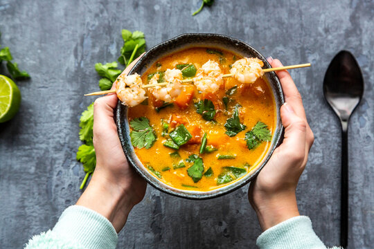 Girl's hands holding bowl of sweet potato soup with shrimps, coconut flakes and fresh coriander