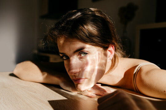 Portrait of young woman leaning on wooden table at sunlight