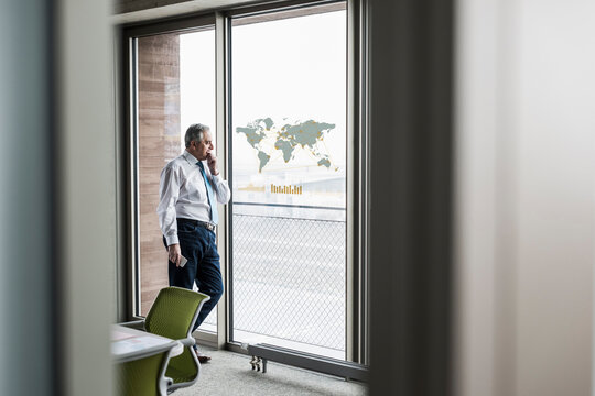 Businessman looking at windowpane with world map in office