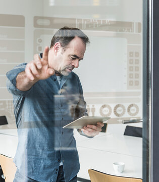 Businessman with tablet touching glass pane with data in office