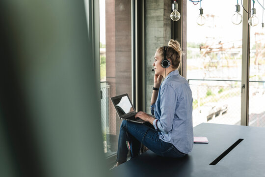 Young businesswoman sitting at desk, making a call, using headset and laptop