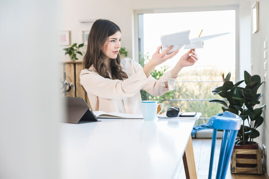 Young woman sitting at table at home holding plane model