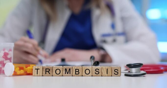 Wooden blocks spell word Trombosis near pills and stethoscope on clinic desk. Doctor writes chart notes checking clot risk factors at appointment