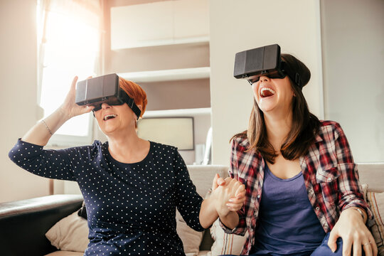 Excited adult daughter with mother at home wearing VR glasses