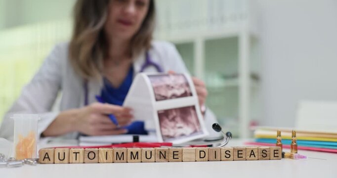 Wooden blocks spell phrase Autoimmune Disease near tools on clinic desk. Lady doctor studies skin photos selecting tests for immune disorder workup