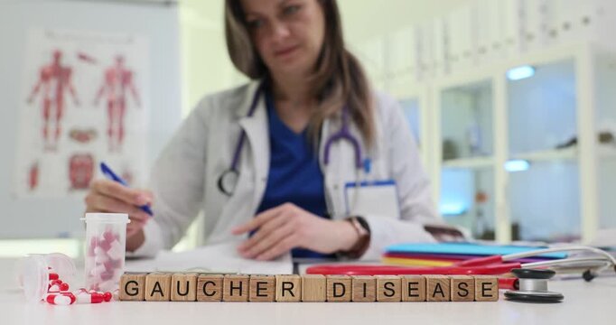 Wooden blocks spell phrase Gaucher Disease on clinic desk. Woman doctor writes notes studying lab papers near stethoscope and pills carefully