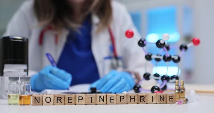 Wooden blocks spell word Norepinephrine near molecule model and vials on lab desk. Doctor mixes dose documenting infusion order for shock care
