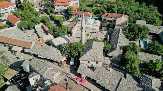 Mostar, Bosnia and Herzegovina 05 28 2025: Arc drone video of Hajji Kurts Mosque with Hamam Museum in Mostar Old Town and Neretva River in the background on a sunny day.