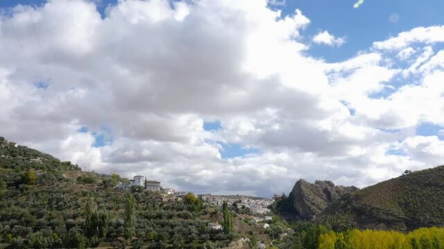 Time-lapse of white clouds over the town of Castril, Granada. Panoramic view of the Spanish hills, olive groves, and autumn poplars.