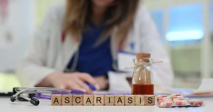 Wooden blocks spell word Ascariasis on busy clinic desk. Doctor writes medical history reviewing antiparasitic tablets for daily patient treatment